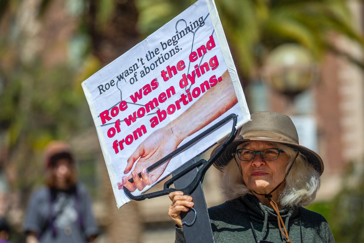 A woman holds hanger with the sign, "Roe wasn't the beginning of abortions. Roes was the end of women dying from abortions."