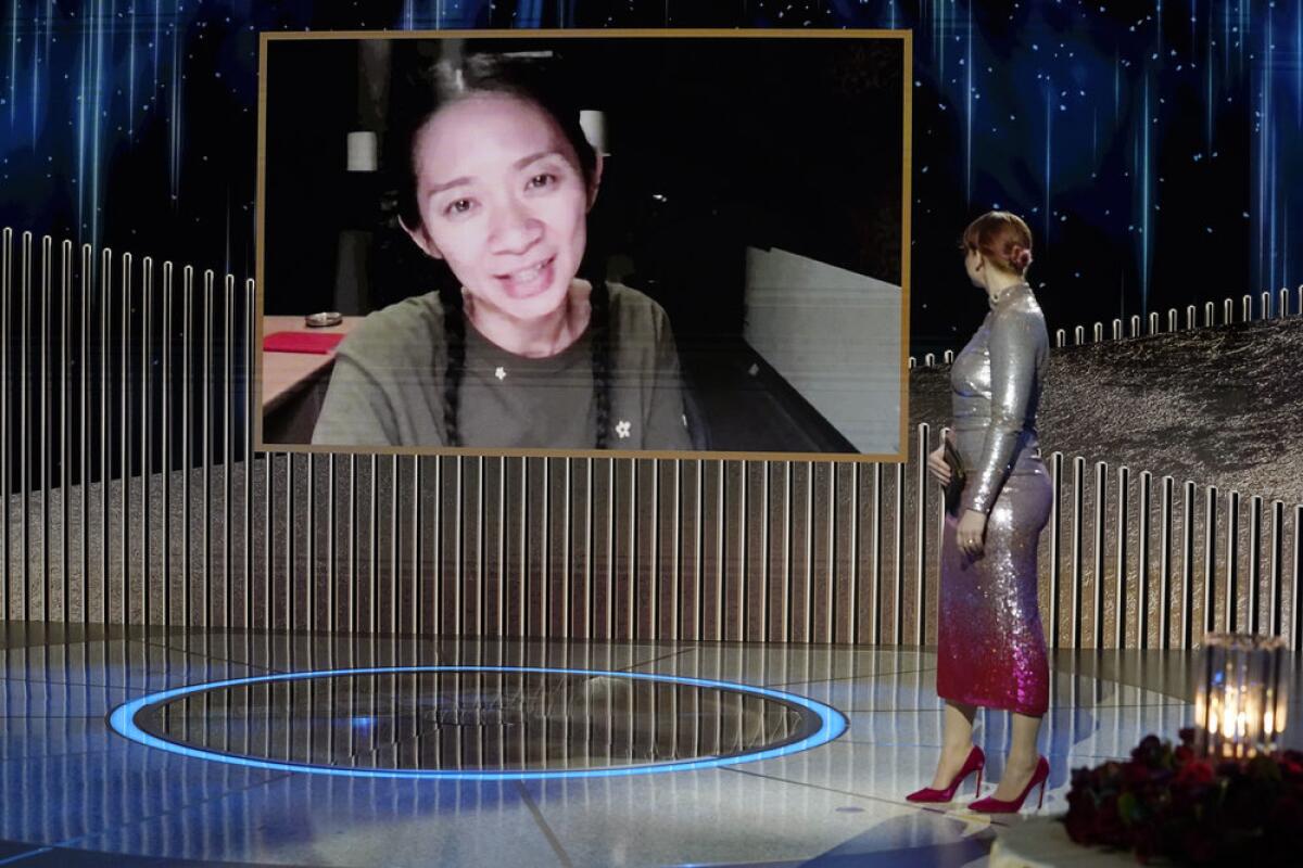 A woman accepts an award on a giant video screen while another woman stands on stage in front of the screen 