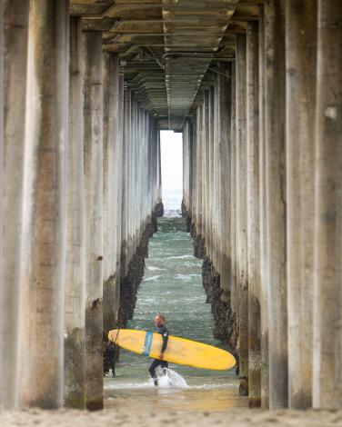 A surfer prepares to enter the water next to the pier at Huntington City Beach, in Huntington Beach, on Thursday, April 30, 2020. California Gov. Gavin Newsom said all state and local beaches in Orange County must close.