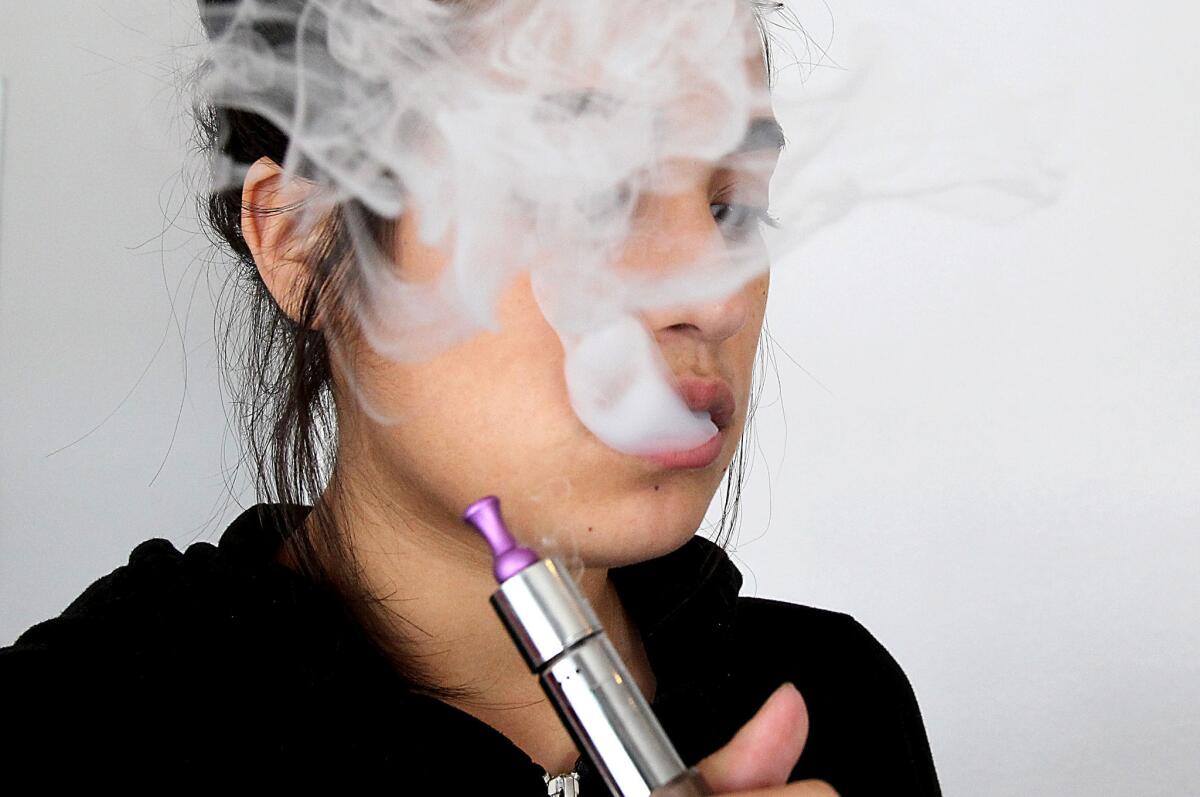 Maria Valencia uses an electronic cigarette to vaporize a nicotine solution at Vaping Ape, an e-cigarette retailer in Hollywood. Hours after the L.A. City Council voted to ban the use of electronic cigarettes in bars, restaurants, nightclubs and other public areas, the city of Long Beach passed its own restrictions.