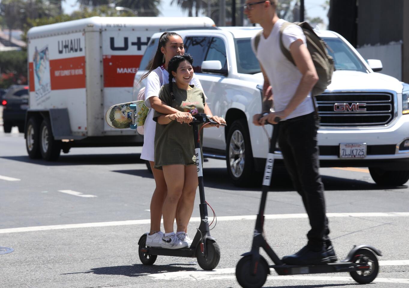 Girls ride across Pacific Avenue on a single Bird scooter as another Bird rider crosses their path in Venice on July 5, 2018. Double riders and riding without helmets are illegal when using the Bird scooter. According to the Bird rental agreement, riders must be 18 years old to operate the scooters.