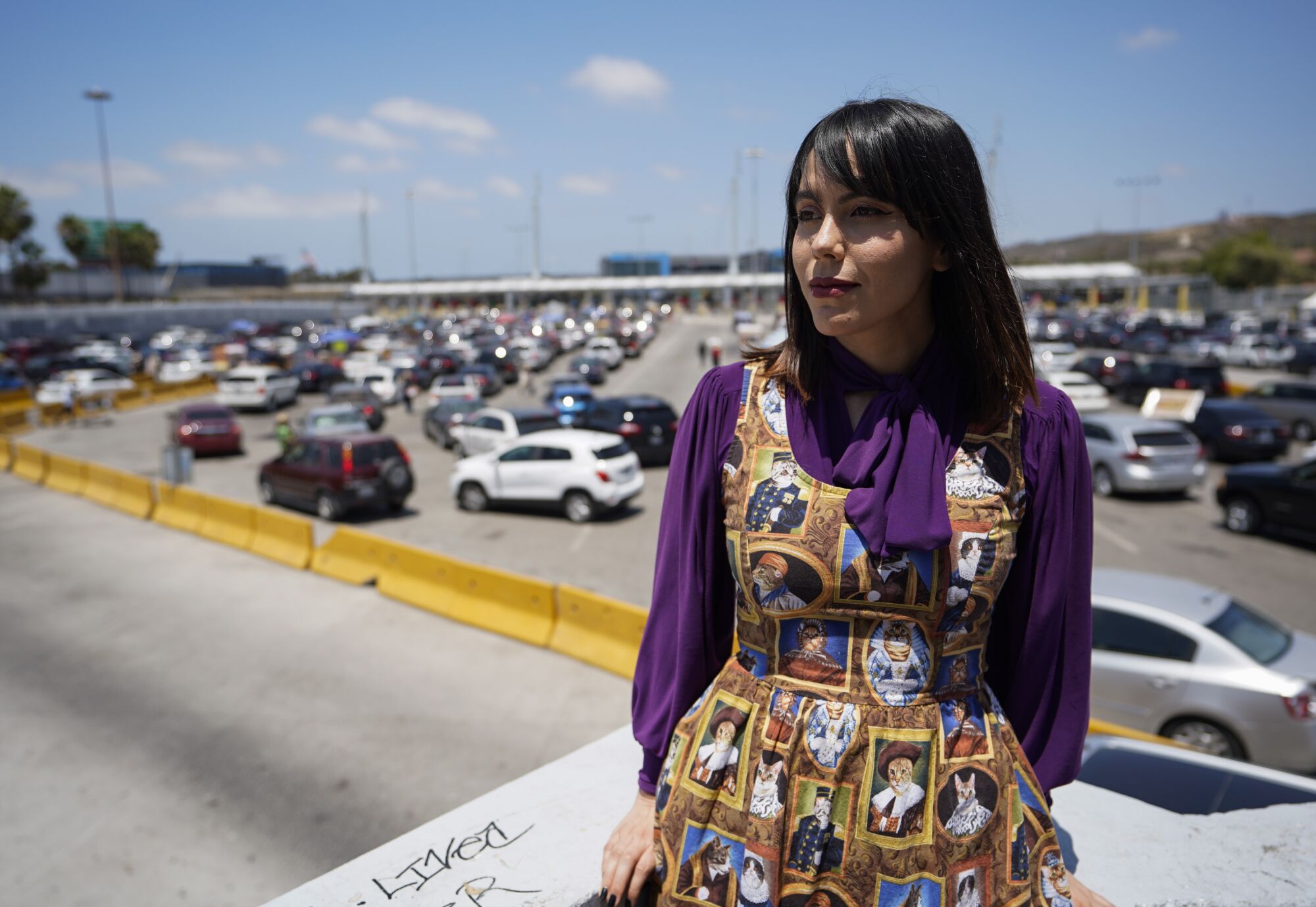 Estefania Castañeda Pérez poses for a portrait on a ledge overlooking lines of cars waiting at the San Ysidro border crossing