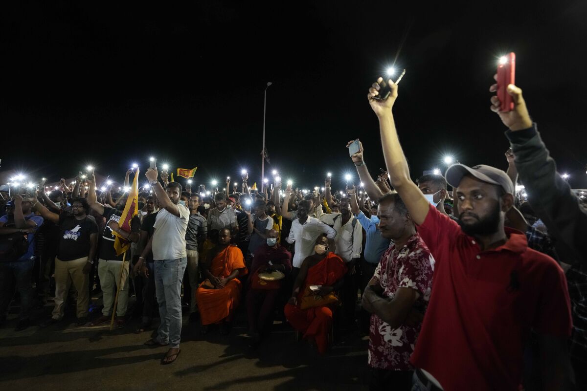 Sri Lankans hold up their mobile phone torches during a vigil condemning police shooting at protesters in Rambukkana, 90 kilometers (55 miles) northeast of Colombo, at a protest outside the president's office in Colombo, Sri Lanka, Tuesday, April 19, 2022. Sri Lankan police opened fire Tuesday at a group of people protesting new fuel price increases, killing one and injuring 10 others, in the first shooting by security forces during weeks of demonstrations over the country's worst economic crisis in decades. (AP Photo/Eranga Jayawardena)