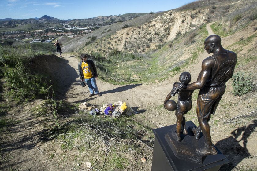 CALABASAS, CA-JANUARY 26, 2022: David Cataldo, 30, of Agoura Hills, visits the crash site in the hills above Las Virgenes Rd in Calabasas that took the lives of Los Angeles Lakers legend Kobe Bryant, his daughter Gianna, and 7 others exactly 2 years ago, on January 26, 2020. In foreground is a bronze statue of Bryant and his daughter Gianna. The statue, weighing about 160 pounds including the steel pedestal, was made by sculptor Dan Medina of West Hills, who had to carry the statue in sections, for the just over 1 mile hike to the crash site. He started out, using a cart and then the cart broke, forcing him to carry it to the crash site. (Mel Melcon / Los Angeles Times)