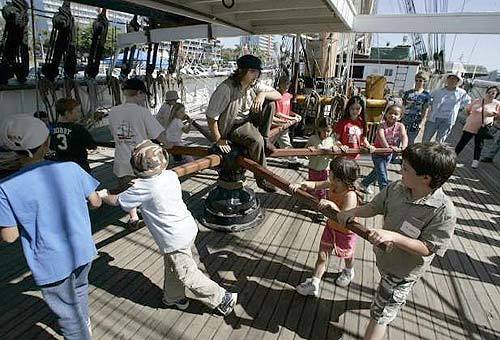 Crew member Ben Cuatt, in period garb, leads the younger folks in cranking the sail-raising capstan aboard the Star of India at San Diego's Maritime Museum.