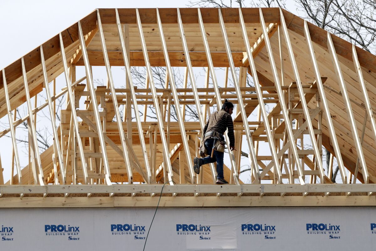 In this March 25, 2020, photo, a construction worker walks along a roof on a new home.