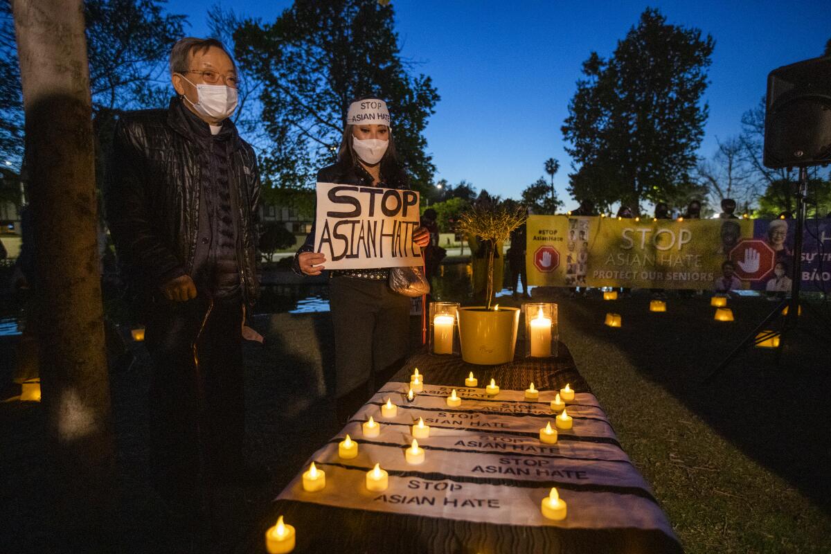 Vanessa Nguyen, center, of Irvine, holds a Stop Asian Hate sign while joining community leaders praying.