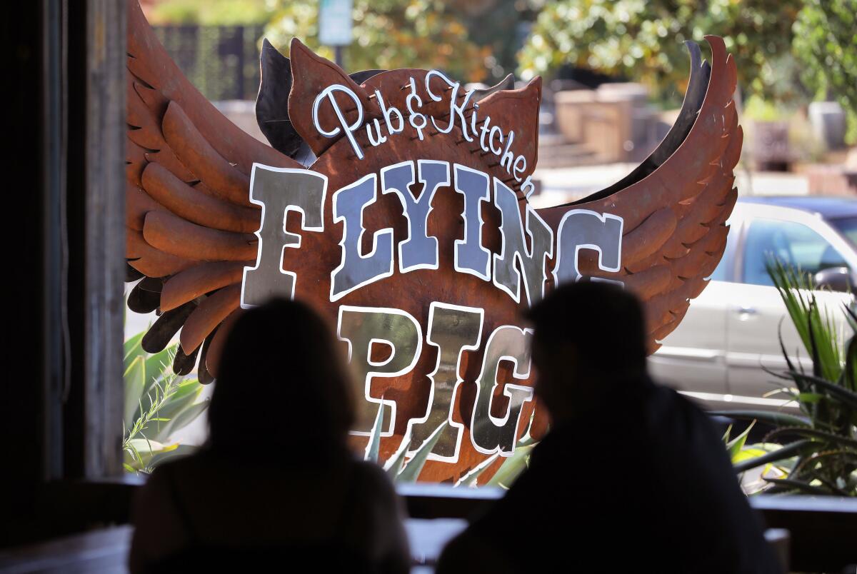 Owners Aaron and Roddy Browning silhouetted in front of the monument sign for their Vista restaurant Flying Pig Pub & Kitchen. The restaurant will be revamped and re-branded in September as the more casual TownHall Public House.