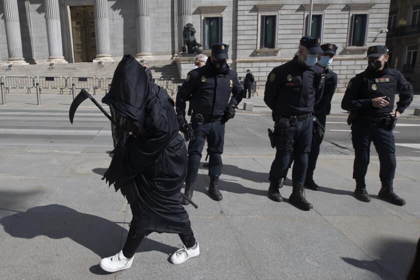 An anti Euthanasia protester walks in front of police officers outside the Spanish Parliament in Madrid, Spain, Thursday, March 18, 2021. Spain has become the seventh country in the world and fourth in Europe to allow physician-assisted suicide and euthanasia for long-suffering patients of incurable diseases or unbearable permanent conditions. The parliament's lower house on Thursday gave the final go-ahead to the euthanasia bill in a 202-140 vote with two abstentions. (AP Photo/Paul White)