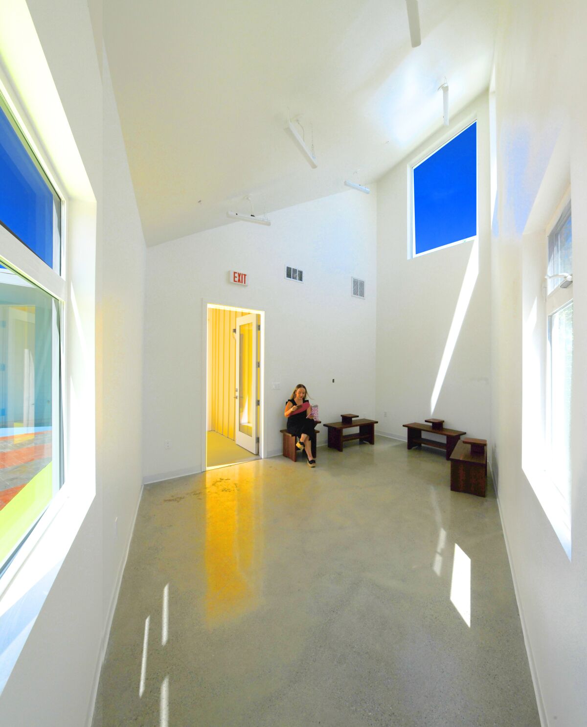 A woman sits in a room with polished concrete floors and cathedral ceilings that meet at a point on one side.