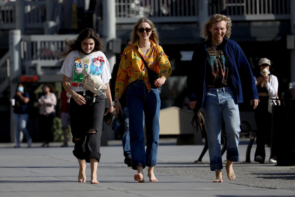Three women walk without masks along the boardwalk in Redondo Beach on Tuesday