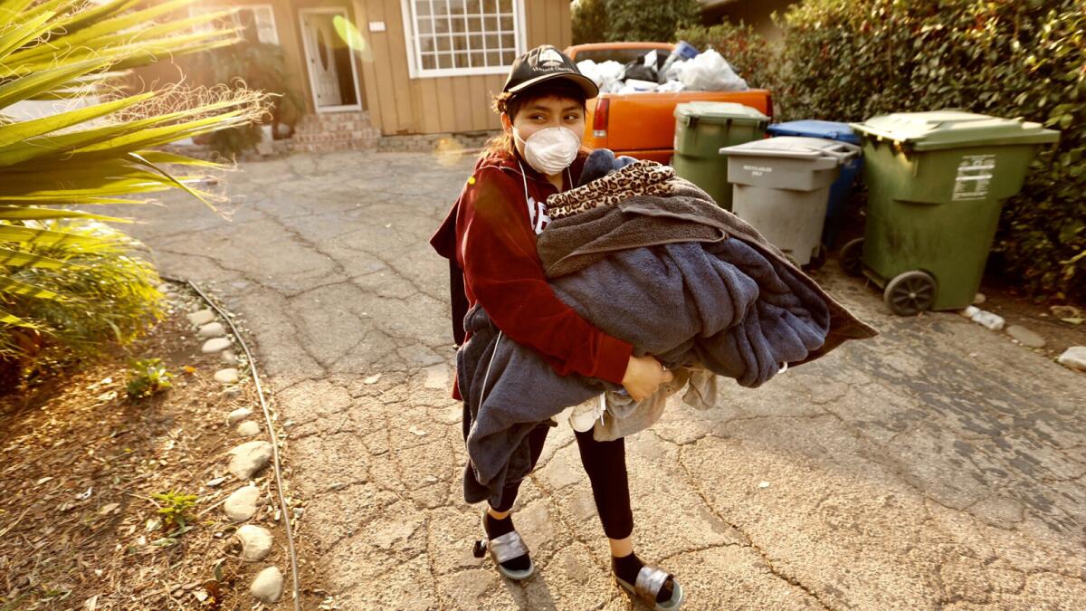 Maria Narvaez carries clothing as she leaves her home on Almon Drive near Hillcrest Drive in Thousand Oaks on Friday morning.
