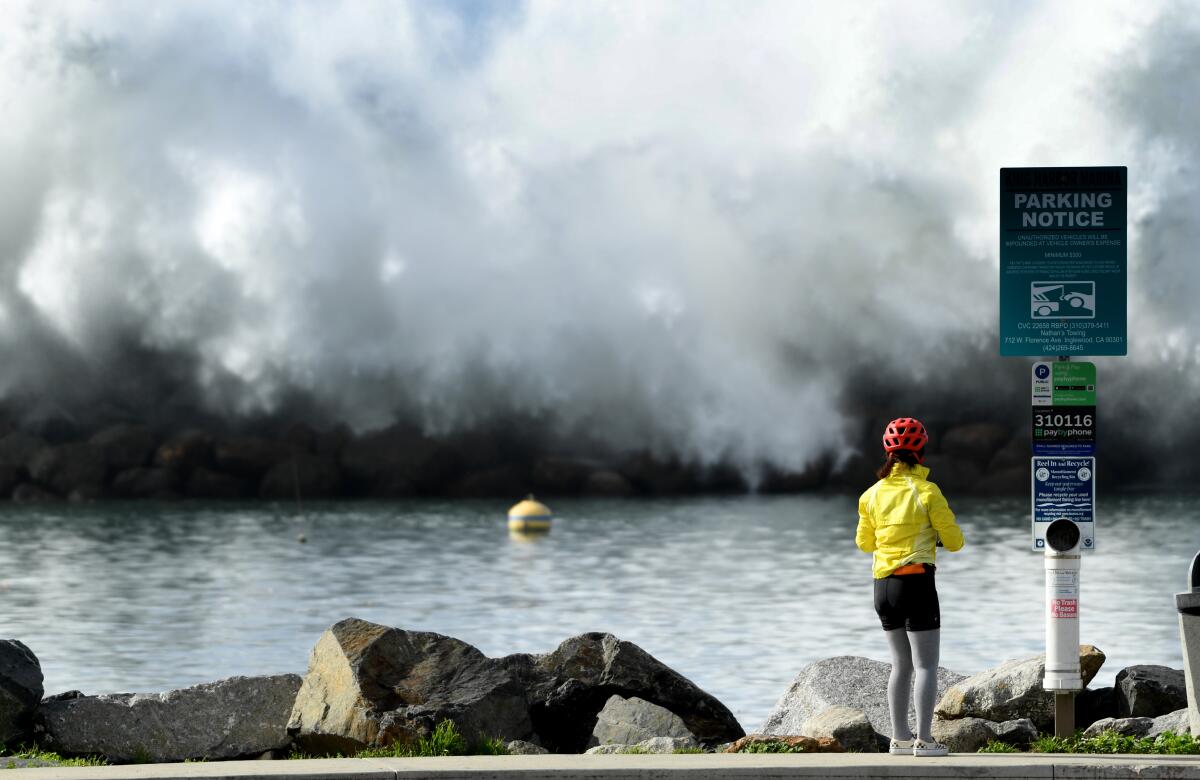A woman watches a wave crash over the Redondo Beach breakwater