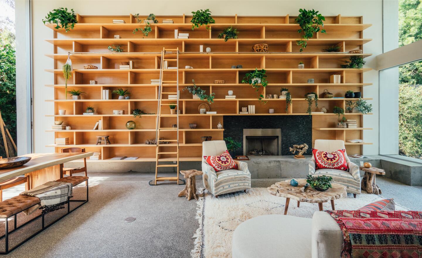 The built-in shelves along one wall have a ladder and living room furniture in front of them.