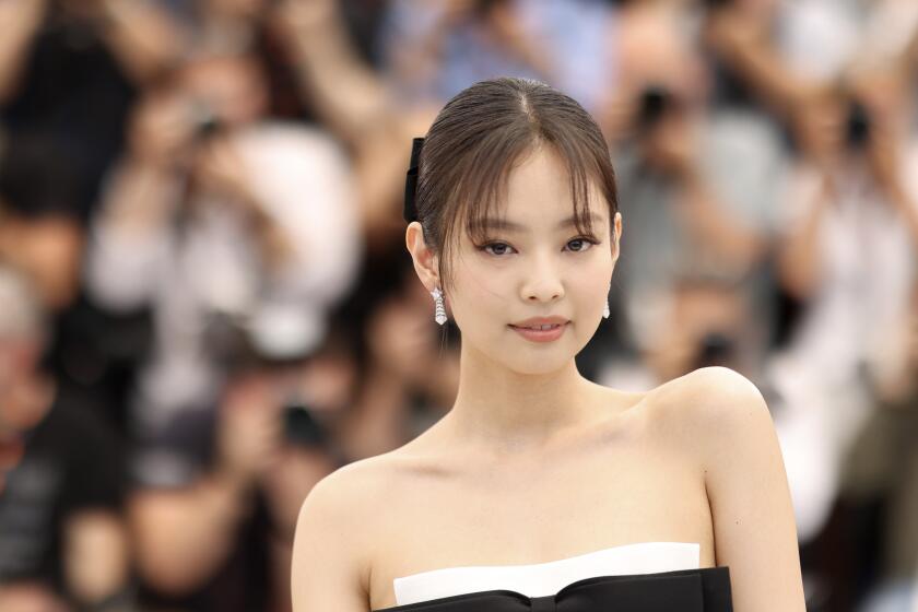 Blackpink's Jennie poses in a sleeveless black-and-white dress and diamond earrings with a crowd blurred out behind her.