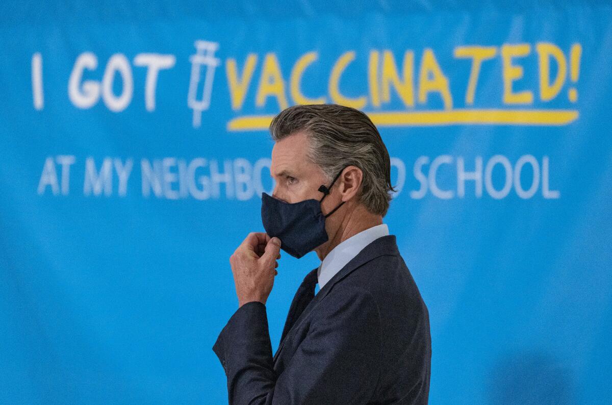 California Gov. Gavin Newsom adjusts his face mask at a news conference.