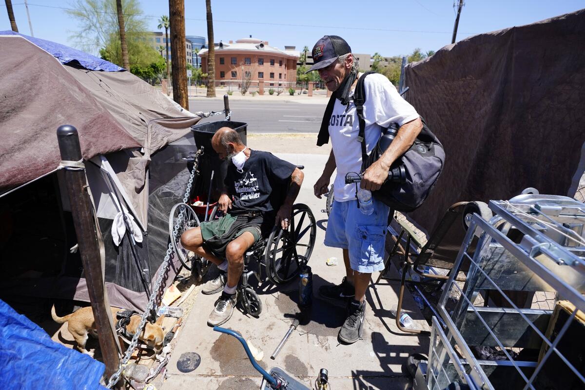 Two men and a dog next to tents on a city sidewalk.