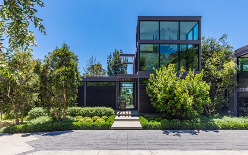 A boxy home with many windows along its sides is surrounded by trees and bushes.