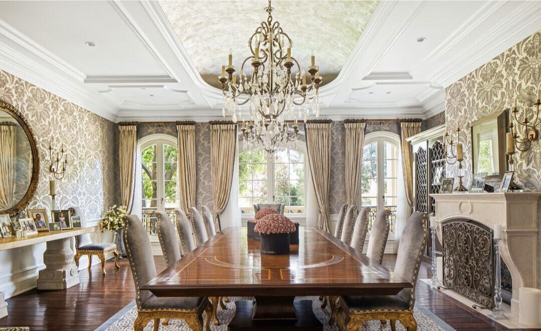 The dining room with a long formal table and chairs, chandelier and windows.