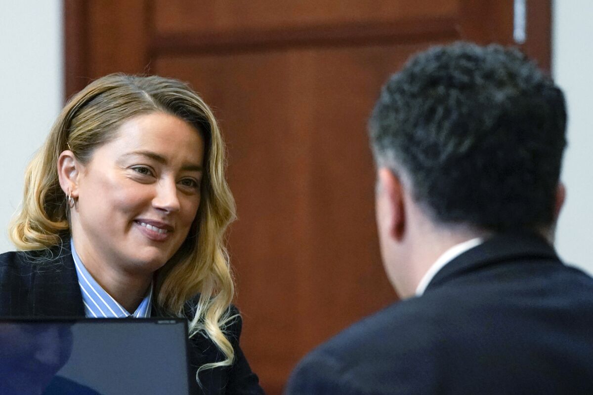 A woman in a courtroom smiles at her attorney, whose back is to the camera.
