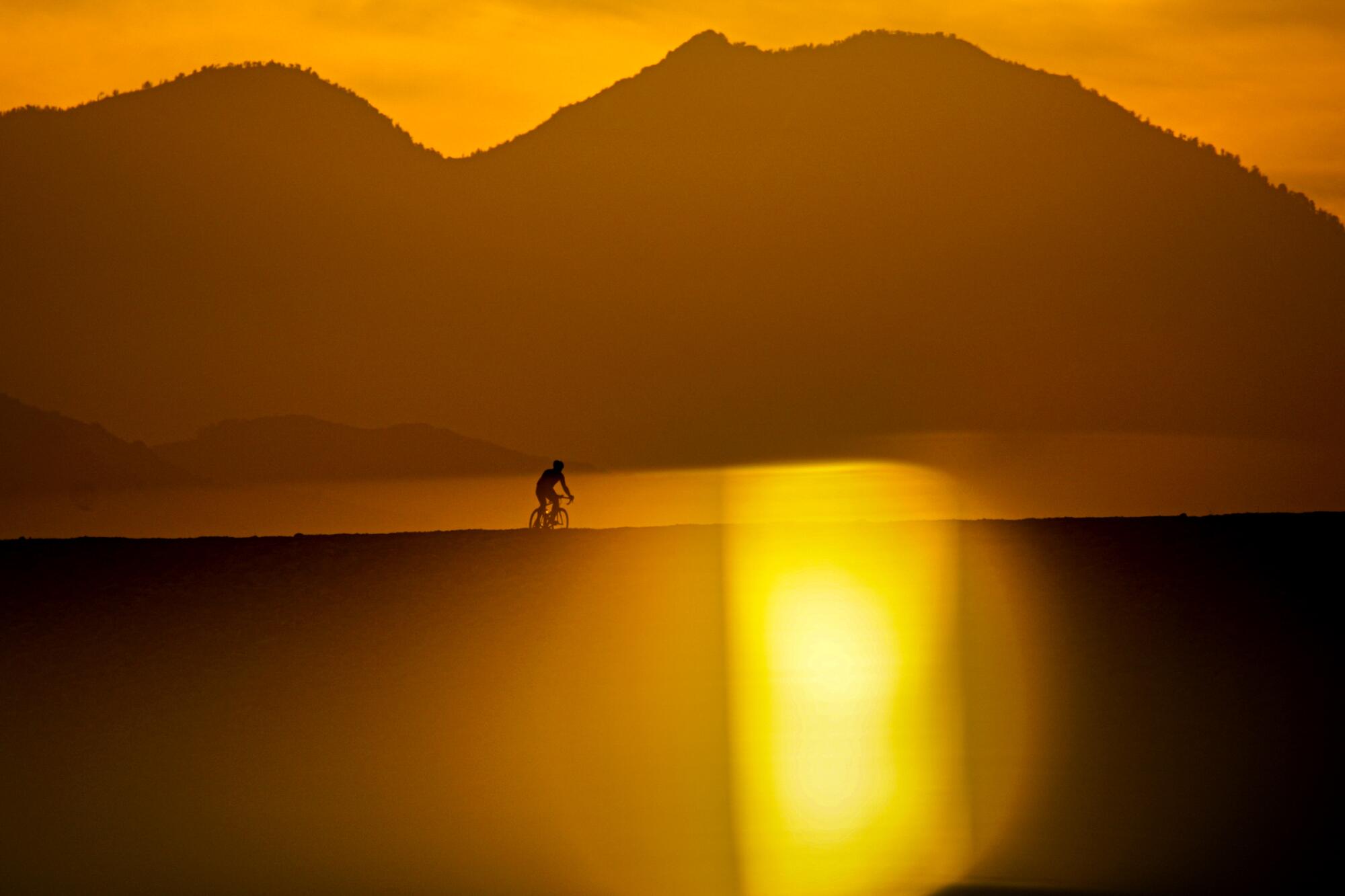 A bicyclist is framed by hills and golden light