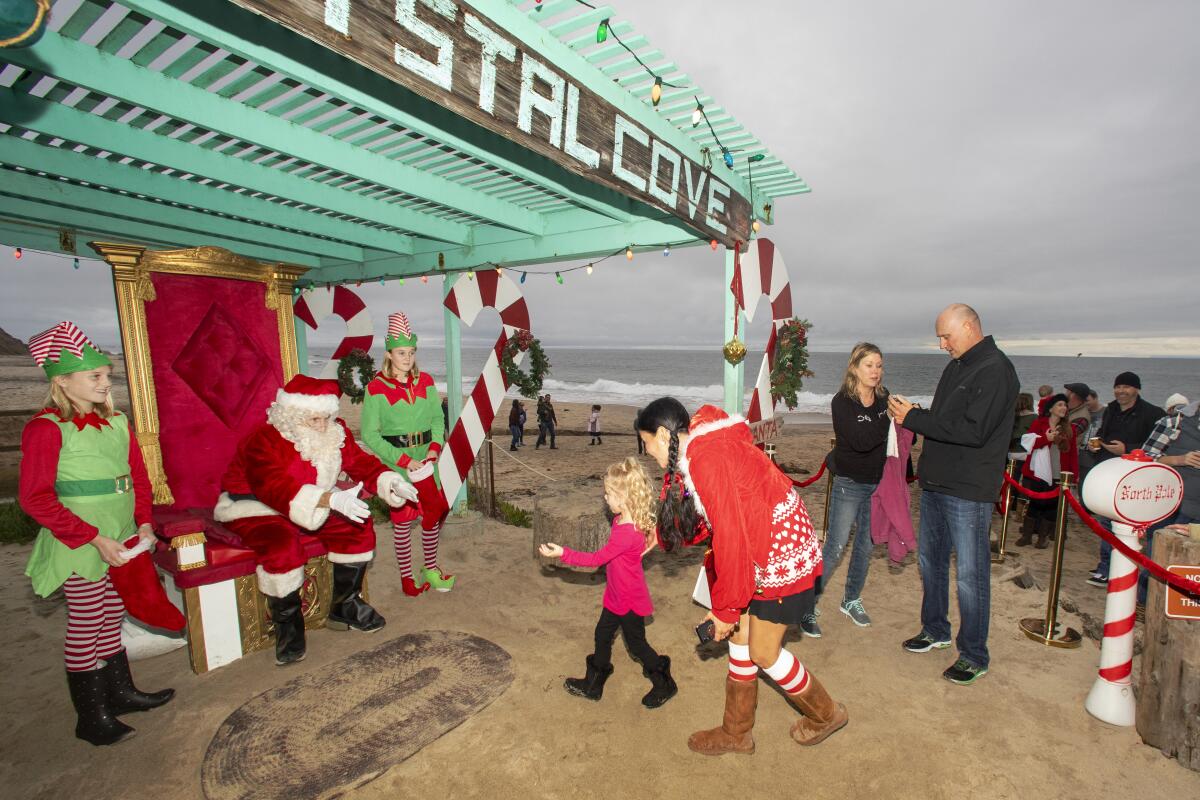 Accompanied by his elves, Santa greets his first young lady as dad prepares to take her picture.