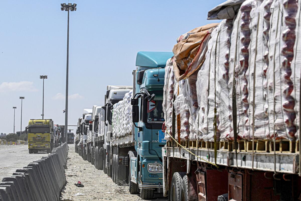 Trucks loaded with supplies are lined up on a dirt road next to a barricade