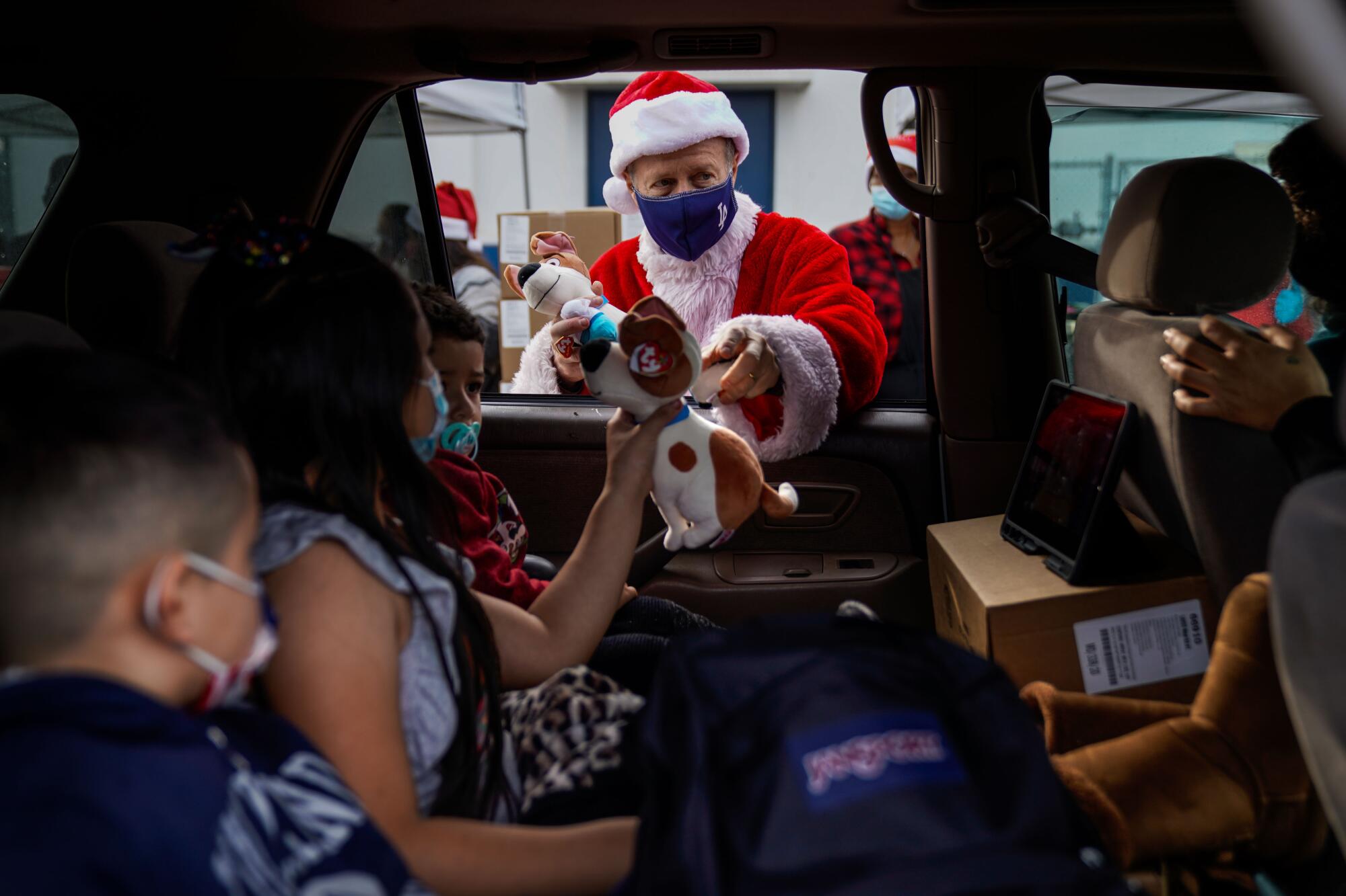 Austin Beutner, dressed as Santa Claus, hands out gifts to kids in a car.