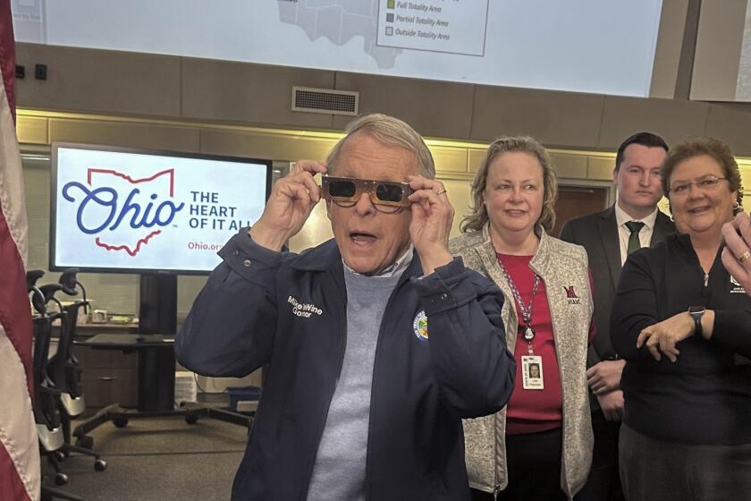 Republican Ohio Gov. Mike DeWine sports a pair of eclipse glasses while talking to reporters at the Ohio Emergency Operations Center in Columbus, Ohio, on Friday, April 5, 2024. DeWine activated the center on Friday to assist communities before, during and after Monday's total solar eclipse, which could draw hundreds of thousands of tourists to the state. (AP Photo/Julie Carr Smyth)