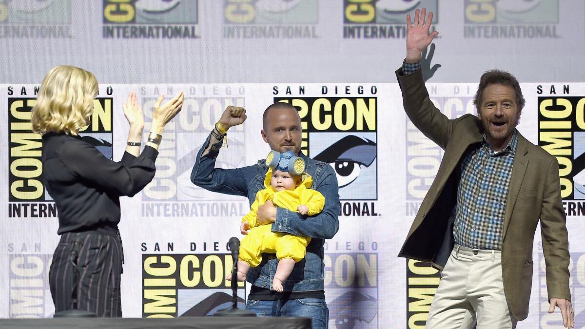 From left to right, Anna Gunn, Aaron Paul with baby Story Annabelle Paul, and Bryan Cranston walk onstage at the "Breaking Bad" 10th anniversary celebration during Comic-Con 2018.
