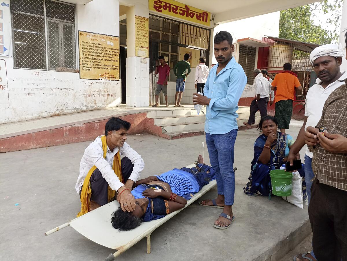 Relatives attend to a patient lying on a stretcher on a concrete sidewalk outside a building