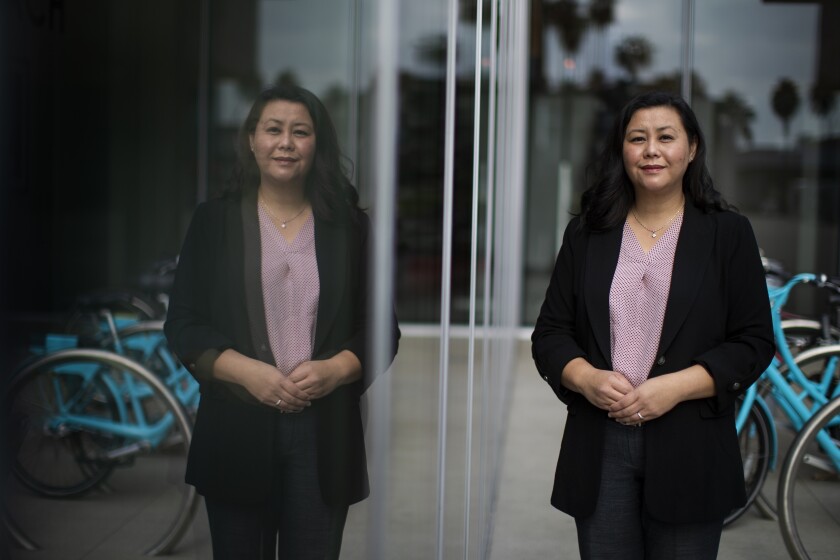 Suely Saro poses for a portrait outside a building, reflected in its glass windows