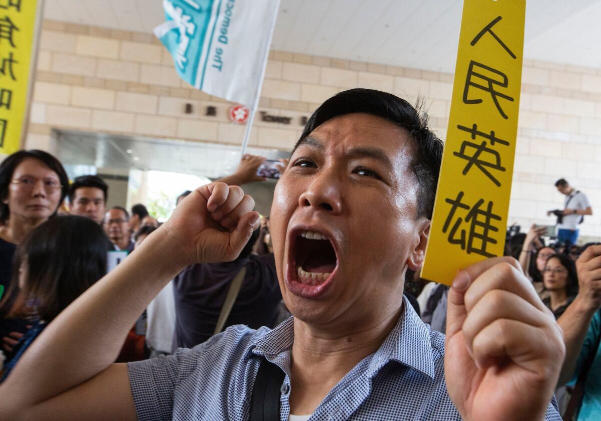 A pro-democracy activist holds a paper saying "People's Hero" and shouts support for activists as they enter court Tuesday.