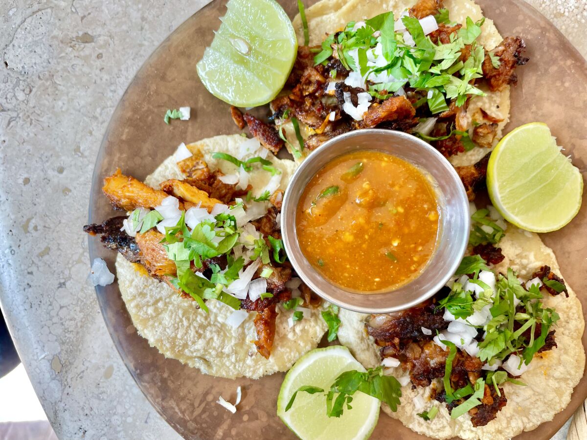 Flat tortillas with chopped lettuce, onion and meat next to sliced limes and a dish of salsa.