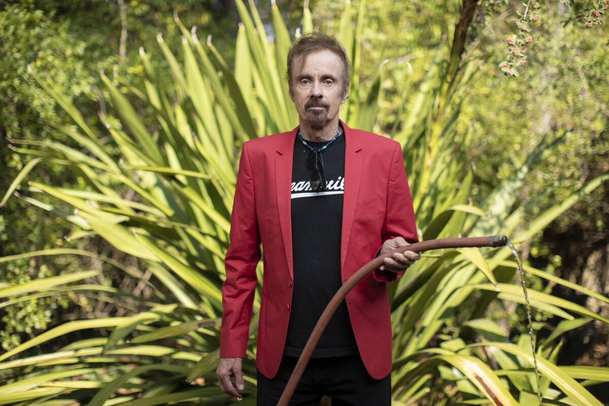 Author T.C. Boyle stands amid plants holding a watering hose.