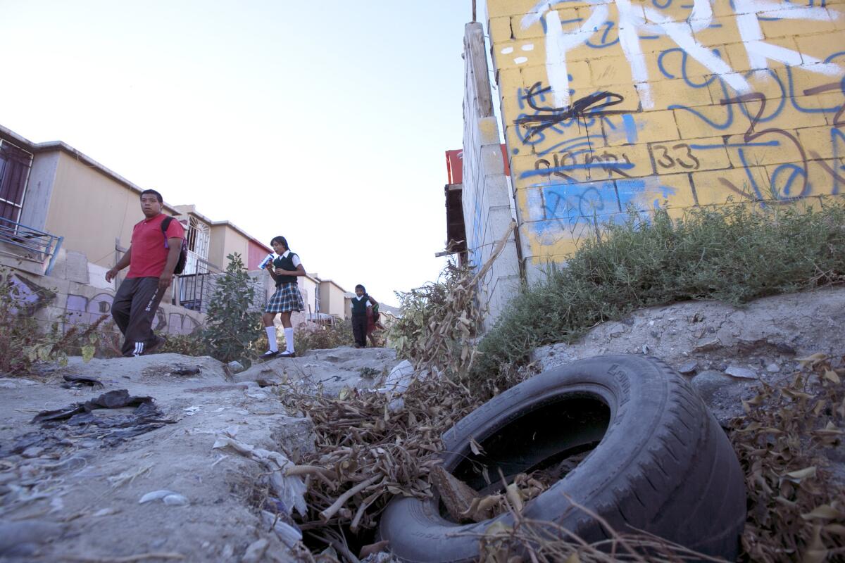 Schoolchildren walk along a trash-filled, rutted alley between row houses in the blighted Cañadas del Florido neighborhood in Tijuana.