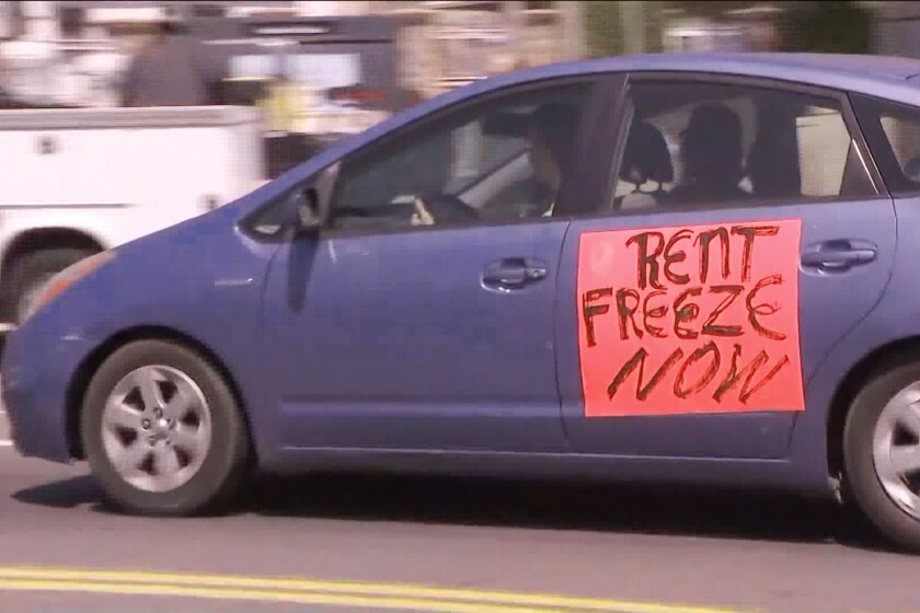 A car with a sign on a door reading "rent freeze now."