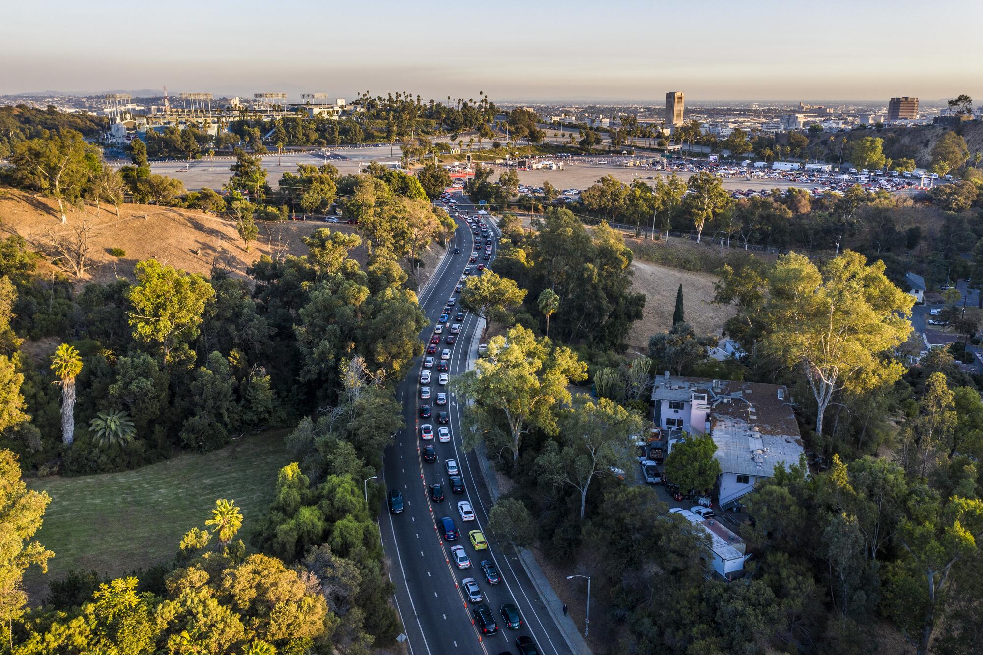 An aerial view shows two lanes packed with cars on a road leading to Dodger Stadium lined with parkland and trees.