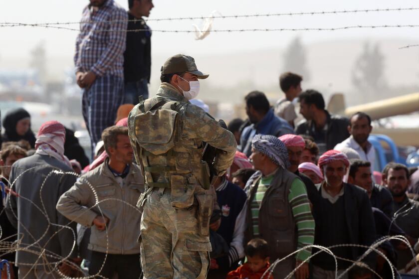 A Turkish soldier stands as Syrians from the town of Kobani wait to enter Turkey at the Yumurtalik border crossing Oct. 2.