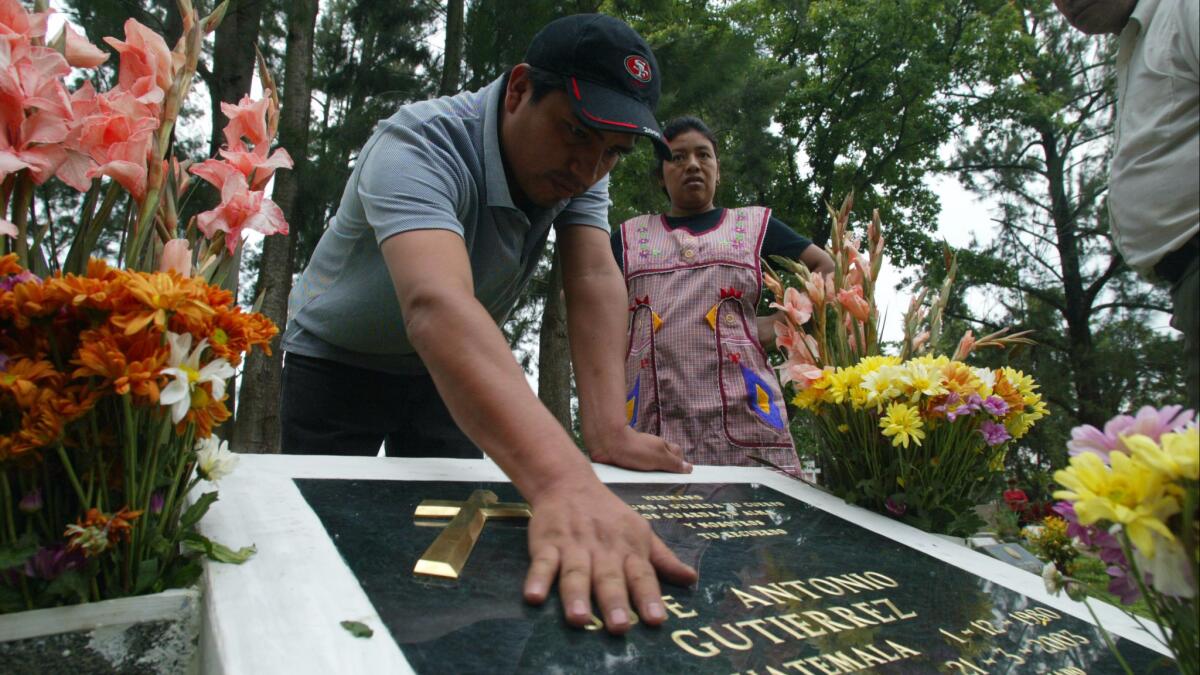 Antonio Paz lays his hand on the headstone of his brother-in-law, slain Marine Jose Antonio Gutierrez, while visiting the grave with his wife, Engracia Cirin, Gutierrez's sister.