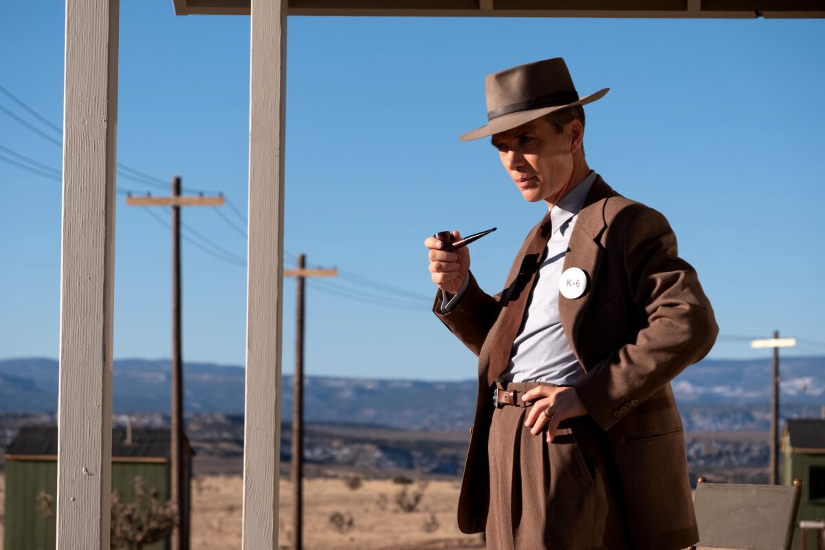A man holding a pipe and wearing a fedora stands on a desert road in "Oppenheimer." 