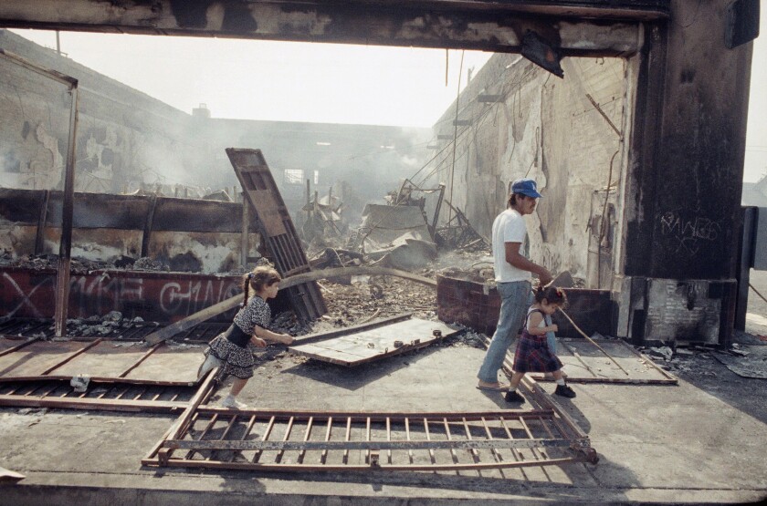 A man and children walk past a burned out building.