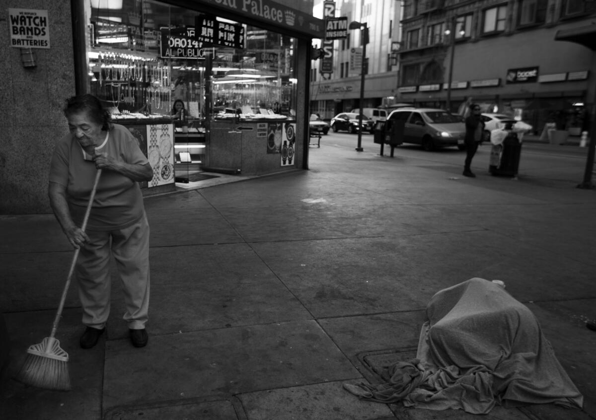 A shopkeeper sweeps around a man sleeping on the sidewalk in the jewelry district.