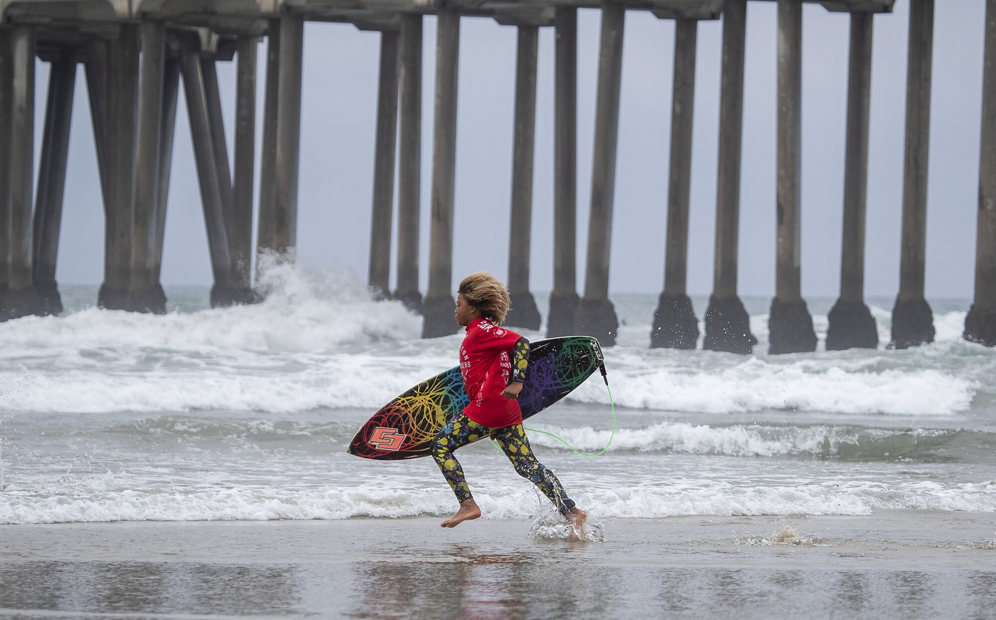 A child with a surfboard runs into the ocean.