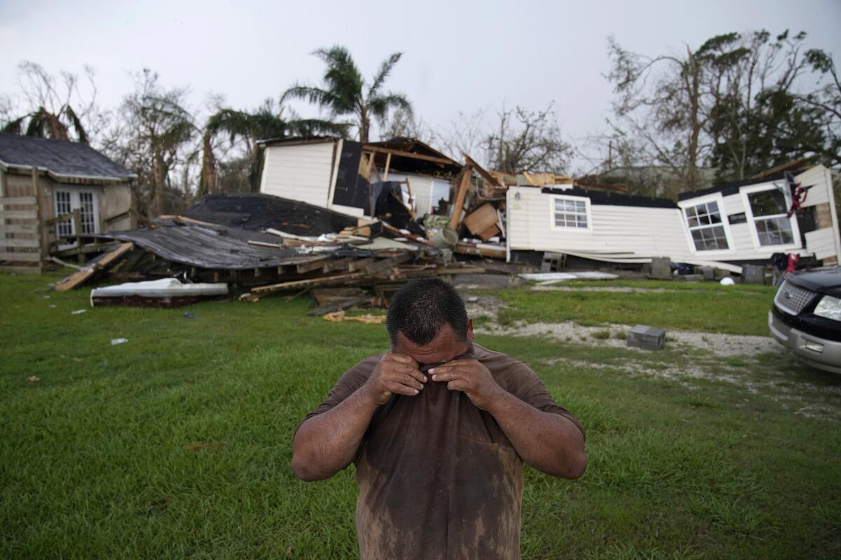 A man stands on a green lawn with rubble in the background.