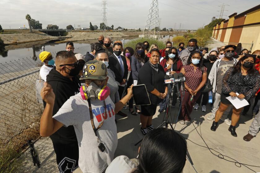 Carson, Los Angeles, California, Oct. 22, 2021-Carson resident Ana Meni, center, speaks during a press conference regarding toxic fumes coming from Dominguez Channel. Ana Meni moved out of her home temporarily due to the smell and is being provided a hotel room by the city. Alejandro Lopez, bottom left, wears a gas mask to protect himself from the toxic fumes. He also evacuated his home. Carson residents and concerned citizens gather beside the Dominguez Channel, where a press conference was held to announce the filing of a lawsuit on behalf of Carson residents sickened by ``sour gas'' hydrogen sulfide air pollution on Oct. 22, 2021. (Carolyn Cole / Los Angeles Times)