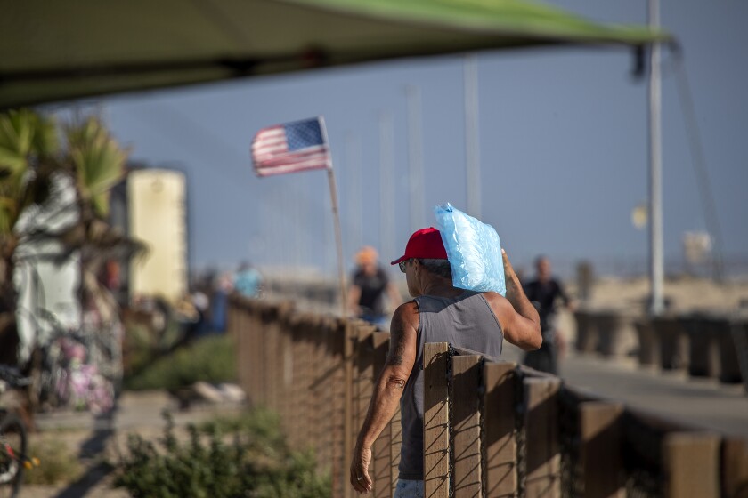 A man walks while carrying a bag of ice on one shoulder. A flag flies in the background.