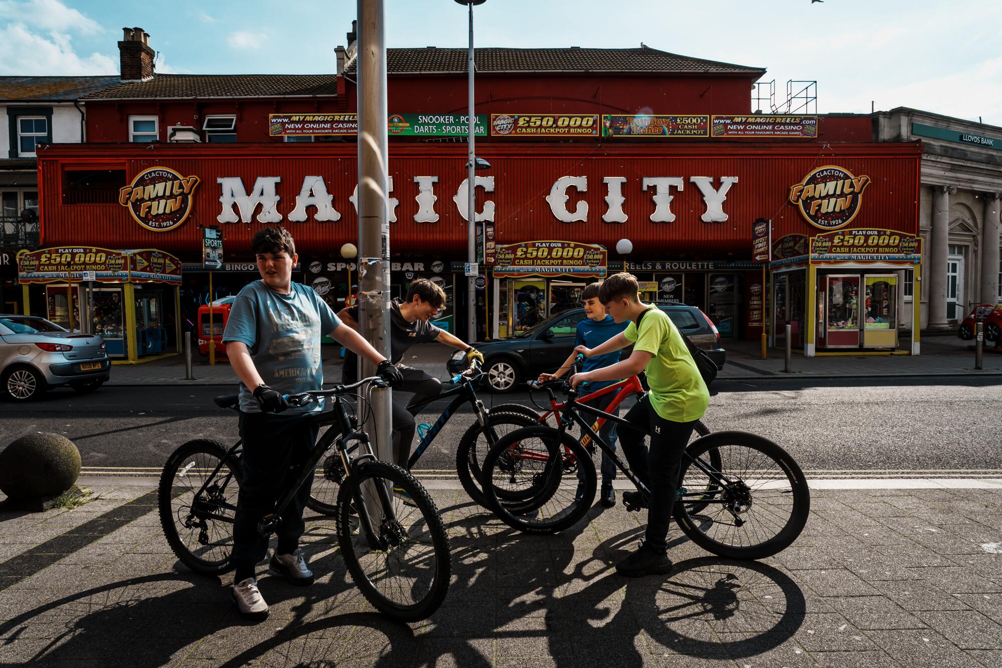 骑着自行车的男孩们在一座挂着“魔术城”标志的建筑对面的人行道上闲逛。 