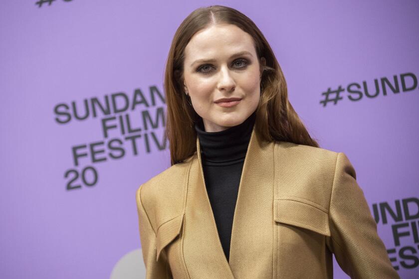 A woman in a jacket and turtleneck poses as she arrives at a film festival