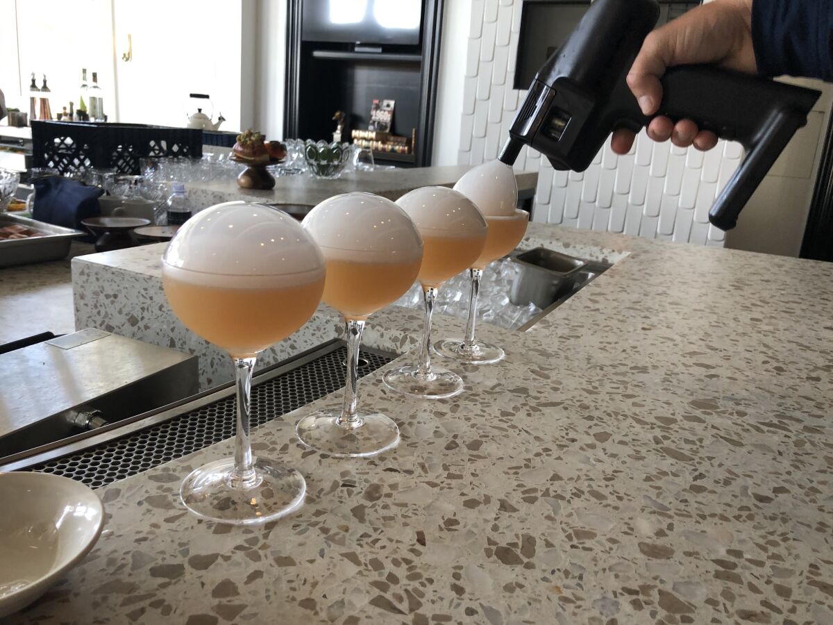 A bartender uses a bubble "gun" to top Smoking Ember cocktails at Ember & Rye restaurant in Carlsbad.
